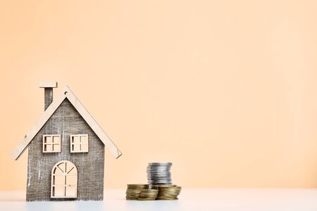 Wooden house model with coins on beige backgroundの写真素材
