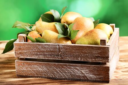 Ripe pears and green leafs in crate on brown wooden tableの写真素材