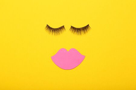 Makeup eyelashes and pink paper lips on yellow background. Minimalism conceptの写真素材