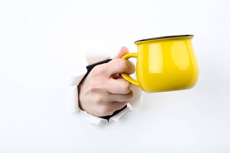 Hand holding yellow mug from white torn paperの写真素材