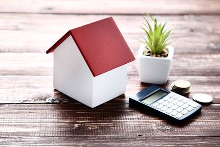 House model with coins and calculator on brown wooden tableの写真素材