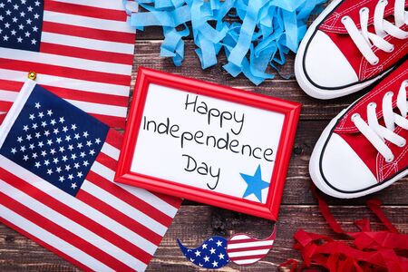 Text Happy Independence Day with american flags and sneakers on wooden table