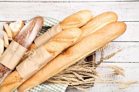 Fresh baguettes with wheat ears on white wooden table