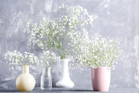 White gypsophila flowers in vases, cup and glass bottle on grey backgroundの写真素材