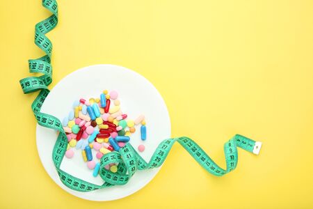 Green measuring tape with pills in plate on yellow backgroundの写真素材