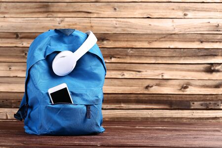 School backpack with headphones and smartphone on brown wooden table