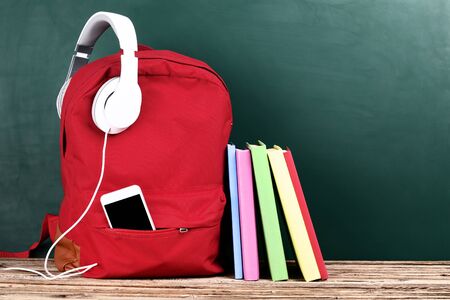 School backpack with headphones, smartphone and books on brown wooden tableの写真素材