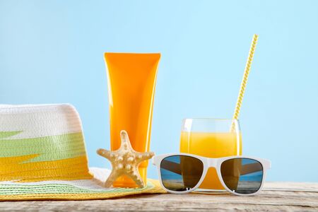 Orange juice with sunscreen, sunglasses and starfish on blue background