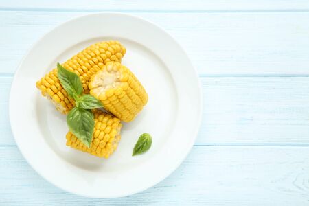 Fresh corn with basil leafs in plate on wooden table