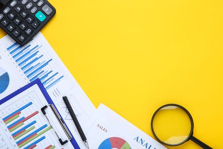 Financial papers with calculator, pen and magnifying glass on yellow backgroundの写真素材