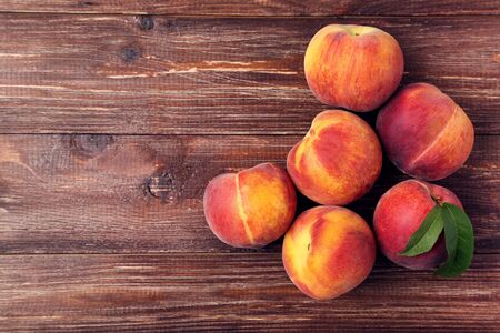 Fresh peaches with green leafs on brown wooden tableの写真素材