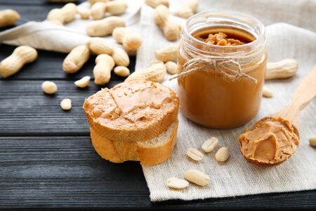 Peanut butter with bread and nuts on black wooden table