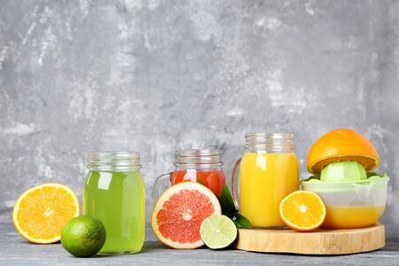 Citrus juice in glass jars with fruits on grey wooden tableの写真素材
