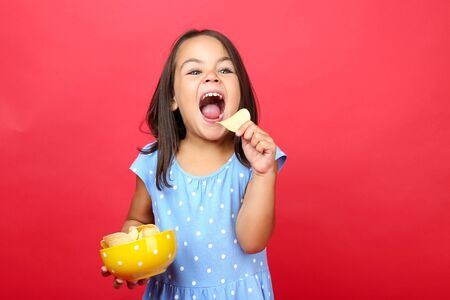 Beautiful little girl with potato chips in bowl on red backgroundの写真素材