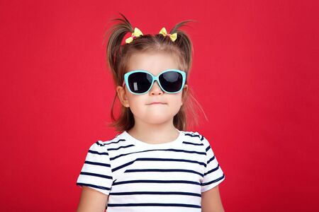 Cute little girl in sunglasses on red backgroundの写真素材