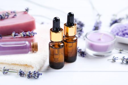 Lavender oil in bottles with flowers, candle and soap on white wooden tableの写真素材