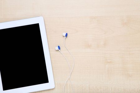 Tablet computer with earphones on wooden table