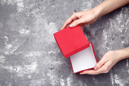 Female hands opening red gift box on grey wooden table