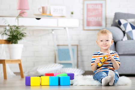 Little boy sitting on white carpet at home and playing with colorful plastic cubes and toy carの写真素材