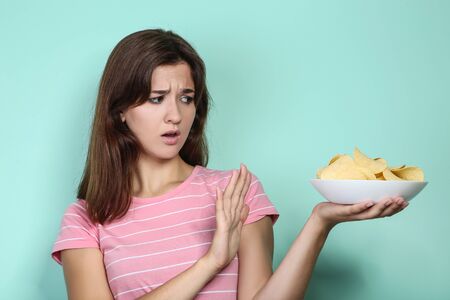Young woman with potato chips in plate on mint backgroundの写真素材