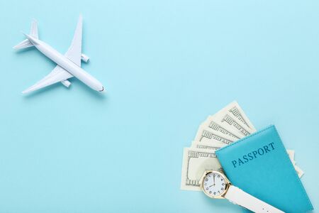 Airplane model with passport, dollar banknotes and wrist watch on blue