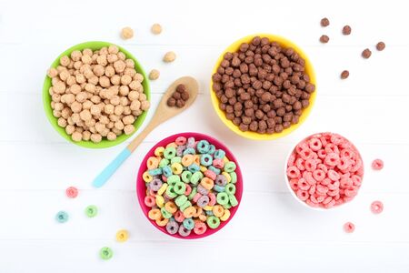 Various corn flakes in bowls with spoon on white wooden table