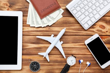 Airplane model with keypad, smartphone, dollar banknotes, compass and tablet computer on brown...