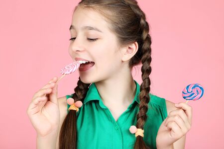 Beautiful young girl eating sweet lollipops on pink backgroundの写真素材