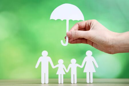 Family figures and female hand holding paper umbrella on green backgroundの写真素材