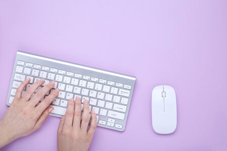 Female hands typing on computer keyboard on purple backgroundの写真素材
