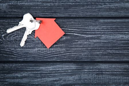 Silver keys with red paper house on black wooden tableの写真素材
