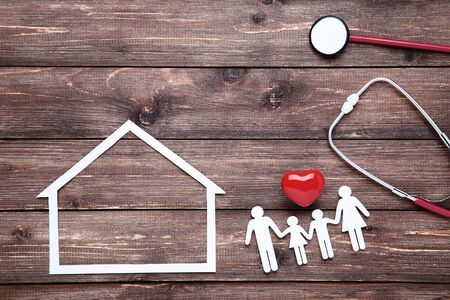 Family figures with red heart, paper house and stethoscope on brown wooden backgroundの写真素材
