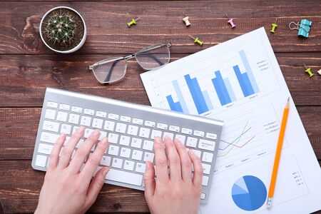 Female hands typing on computer keyboard with diagrams on paperの写真素材