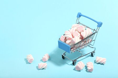 Sweet marshmallows in shopping cart on blue background. Minimalism conceptの写真素材