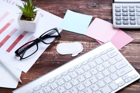 Computer keyboard with office supplies and glasses on brown wooden tableの写真素材