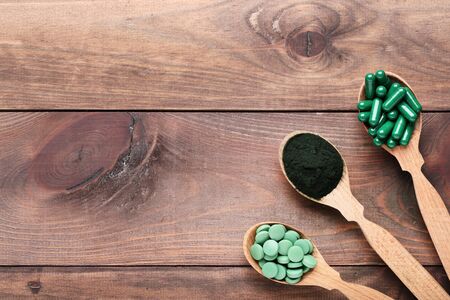 Spirulina powder and tablets in spoons on brown wooden tableの写真素材