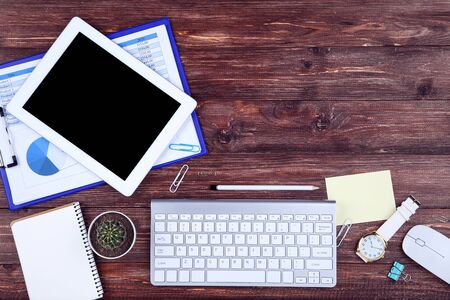 Tablet, keyboard computer with notepad, cactus, mouse and paper charts on brown wooden tableの写真素材