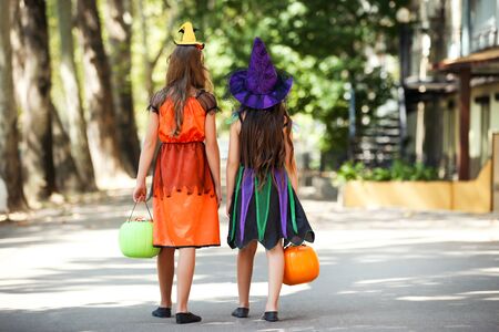 Young girls in halloween costumes with pumkin buckets walking on the streetの写真素材