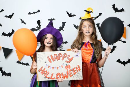 Two young girls in costumes holding paper with text Happy Halloween on white backgroundの写真素材