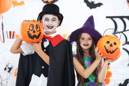 Young girl and boy in halloween costumes with pumpkin bucketsの写真素材