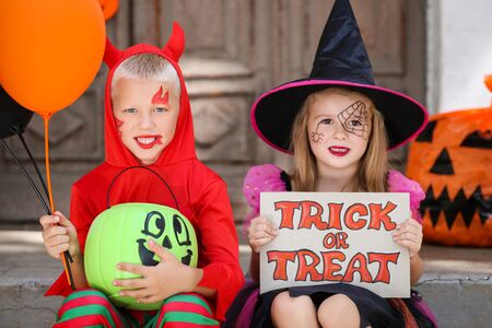 Young girl and boy in halloween costumes sitting on porch with pumpkin buckets and text Trick or Treatの写真素材