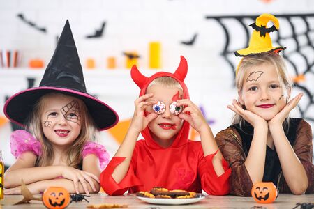 Young girls and boy in halloween costumes sitting by the tableの写真素材