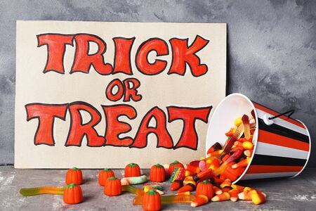Text Trick or Treat with candies in bucket on grey background