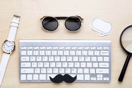 Computer keyboard with sunglasses, magnifying glass and wrist watch on wooden table
