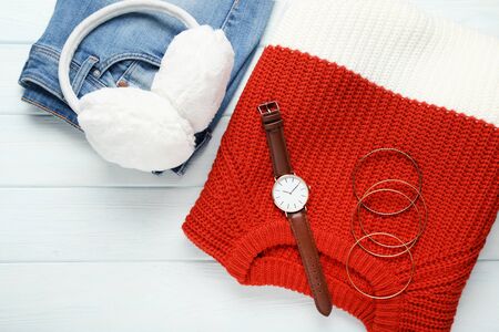 Knitted sweater with jeans, earmuffs and wrist watch on wooden tableの写真素材