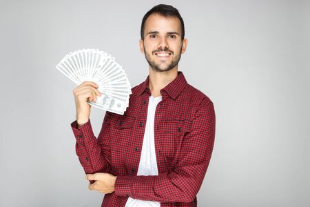 Young happy man holding dollar banknotes on grey backgroundの写真素材