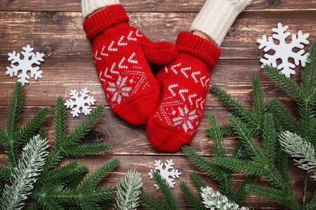 Hands in knitted mittens with snowflakes and fir tree branches on wooden tableの写真素材