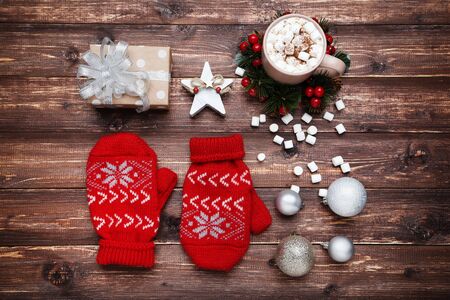 Knitted mittens with gift box, baubles and cup of coffee on brown wooden tableの写真素材
