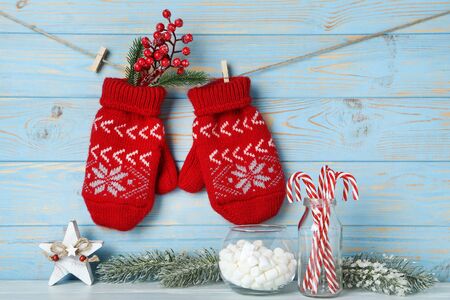 Knitted mittens with fir tree branches, candies, marshamllow and red berries on blue wooden backgroundの写真素材