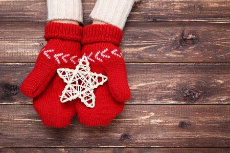 Hands in knitted mittens holding star on brown wooden tableの写真素材
